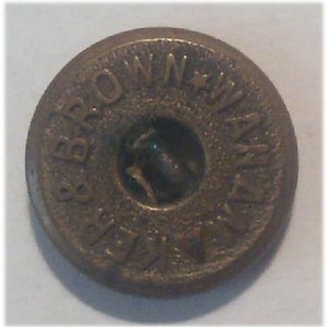 May include: A round, brass-coloured button with the words "Brown Woven" embossed around the edge. The centre of the button has a dark, circular design.