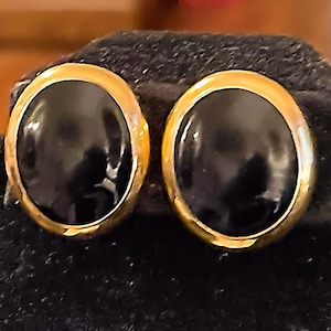 May include: A pair of gold-toned earrings with black oval-shaped stones.