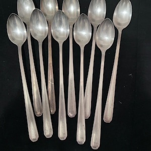 Può includere: Una collezione di dieci cucchiai d'argento disposti su una superficie nera. I cucchiai hanno coppette ovali allungate e manici lunghi e sottili. I cucchiai sono realizzati in un metallo lucido e riflettente, probabilmente argento o una lega color argento.