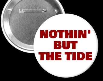 May include: A white button with the text "NOTHIN' BUT THE TIDE" in red, with a silver pin back. The button is round and has a glossy finish. The button is a fan item.