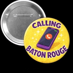 May include: A round pin-back button featuring a yellow background with a purple smartphone illustration in the center. The phone screen displays an orange call icon. The text CALLING BATON ROUGE is printed in purple capital letters around the phone.