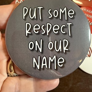 May include: A round, gray button with the text "PUT some RESPECT ON our NAME" in white, bold letters. Other buttons with text are visible in the background.