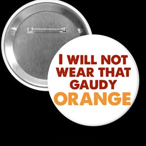 May include: A white button with the text "I WILL NOT WEAR THAT GAUDY ORANGE" in red and orange. The button has a metal pin back and a silver metal rim.