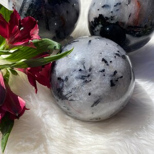 May include: Three black tourmaline spheres on a white fluffy surface. The spheres are clear with black inclusions and have a glossy finish.