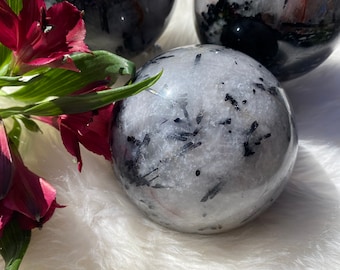 May include: Three black tourmaline spheres on a white fluffy surface. The spheres are clear with black inclusions and have a glossy finish.
