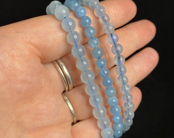 May include: Three blue aquamarine beaded bracelets stacked on top of each other. The beads are round and have a translucent appearance.