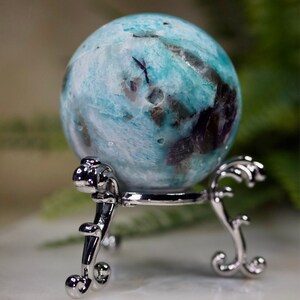 May include: A blue and white sphere with black and brown inclusions, resting on a silver metal stand with ornate details.
