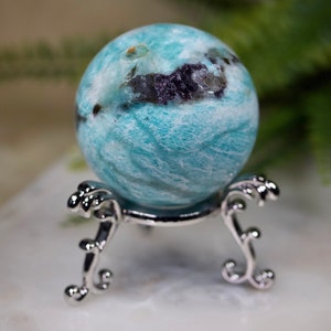May include: A blue and white agate sphere on a silver stand. The sphere has a swirling pattern and some black inclusions.
