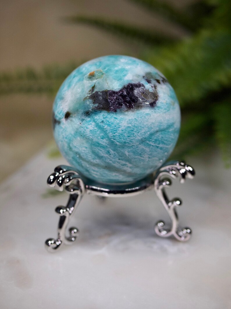 May include: A blue and white agate sphere on a silver stand. The sphere has a swirling pattern and some black inclusions.