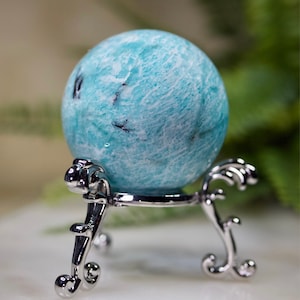 May include: A blue and white amazonite sphere on a silver stand. The sphere is smooth and polished, with a swirling pattern of white and blue.