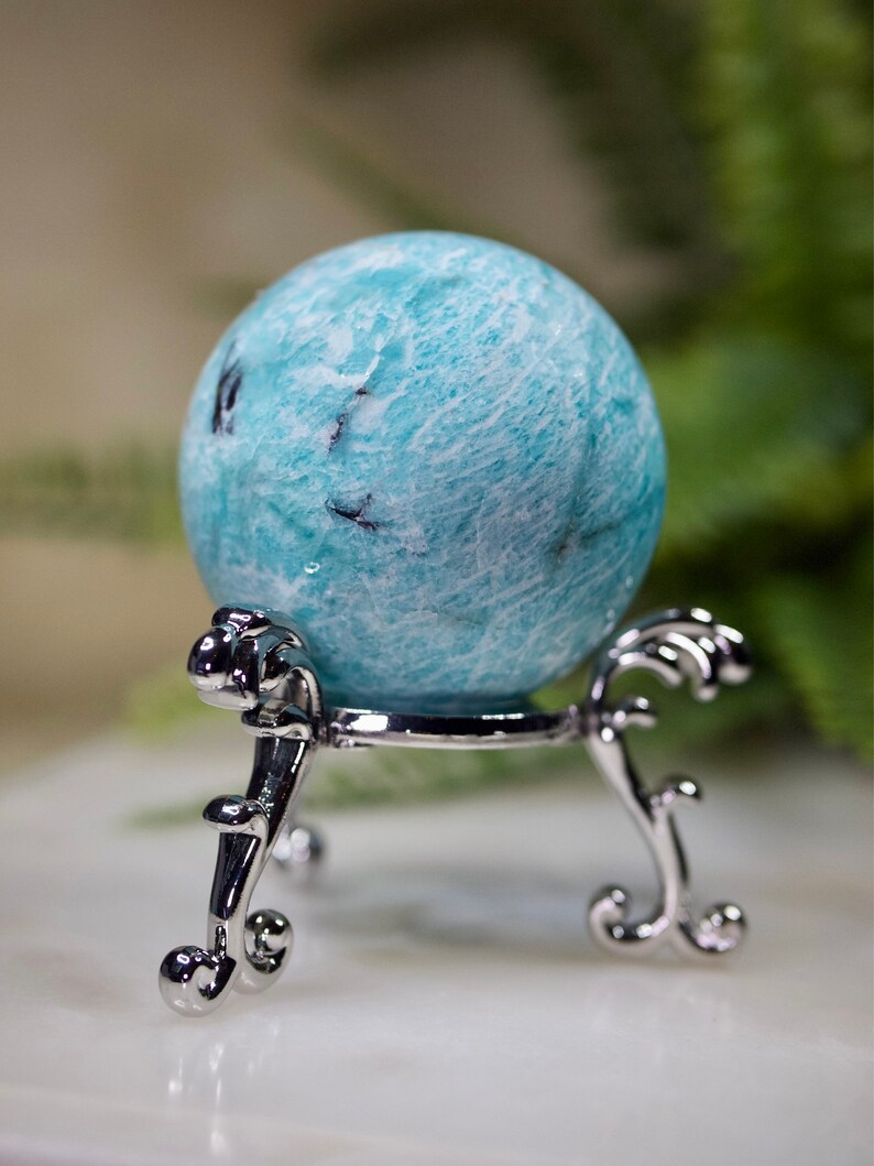 May include: A blue and white amazonite sphere on a silver stand. The sphere is smooth and polished, with a swirling pattern of white and blue.