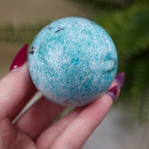May include: A smooth, light blue and white sphere of Amazonite crystal. The sphere has a natural, textured surface.