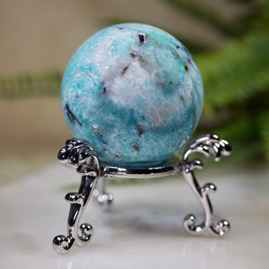 May include: A blue and white amazonite sphere on a silver stand. The sphere has a swirling pattern and black inclusions.