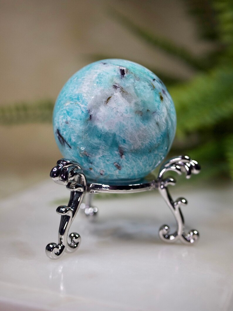 May include: A blue and white amazonite sphere on a silver stand. The sphere has a swirling pattern and black inclusions.