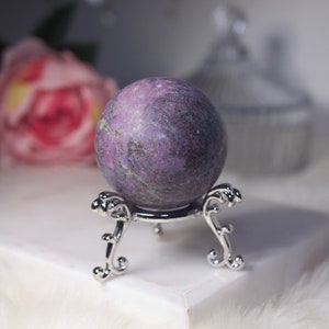 May include: A purple and grey gemstone sphere on a silver stand. The sphere is smooth and polished, with a swirling pattern of purple and grey.