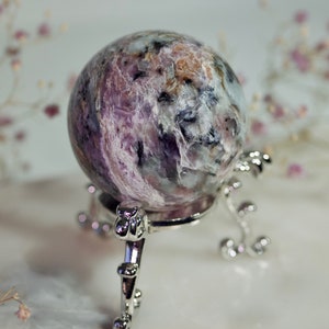 May include: A purple and white crystal sphere on a silver stand. The sphere has a swirling pattern of purple, white, and black.