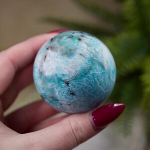 May include: A smooth, round, blue and white crystal sphere. The sphere has a swirling pattern of white and blue.
