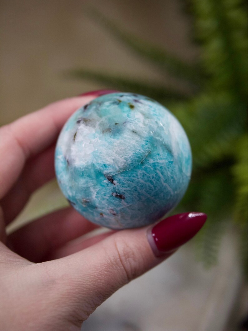 May include: A smooth, round, blue and white crystal sphere. The sphere has a swirling pattern of white and blue.