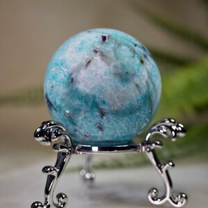 May include: A blue and white crystal sphere on a silver stand. The sphere has a swirling pattern and is polished to a smooth finish.