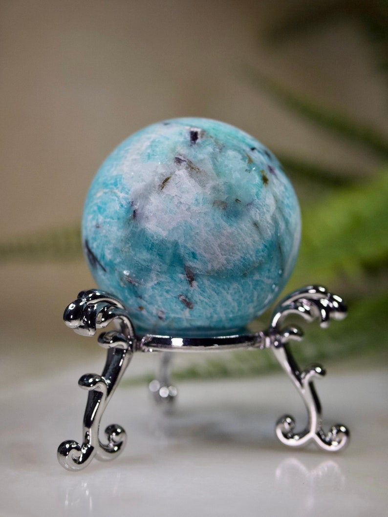May include: A blue and white crystal sphere on a silver stand. The sphere has a swirling pattern and is polished to a smooth finish.
