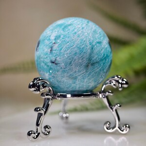 May include: A blue and white amazonite sphere on a silver stand. The sphere is smooth and polished, with a swirling pattern.