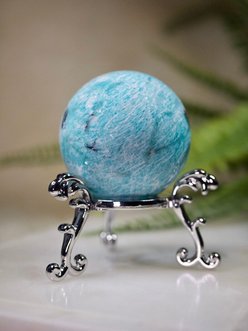 May include: A blue and white amazonite sphere on a silver stand. The sphere is smooth and polished, with a swirling pattern.