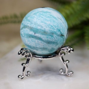 May include: A blue and white sphere of polished amazonite on a silver stand. The sphere has a swirling pattern of white and blue.