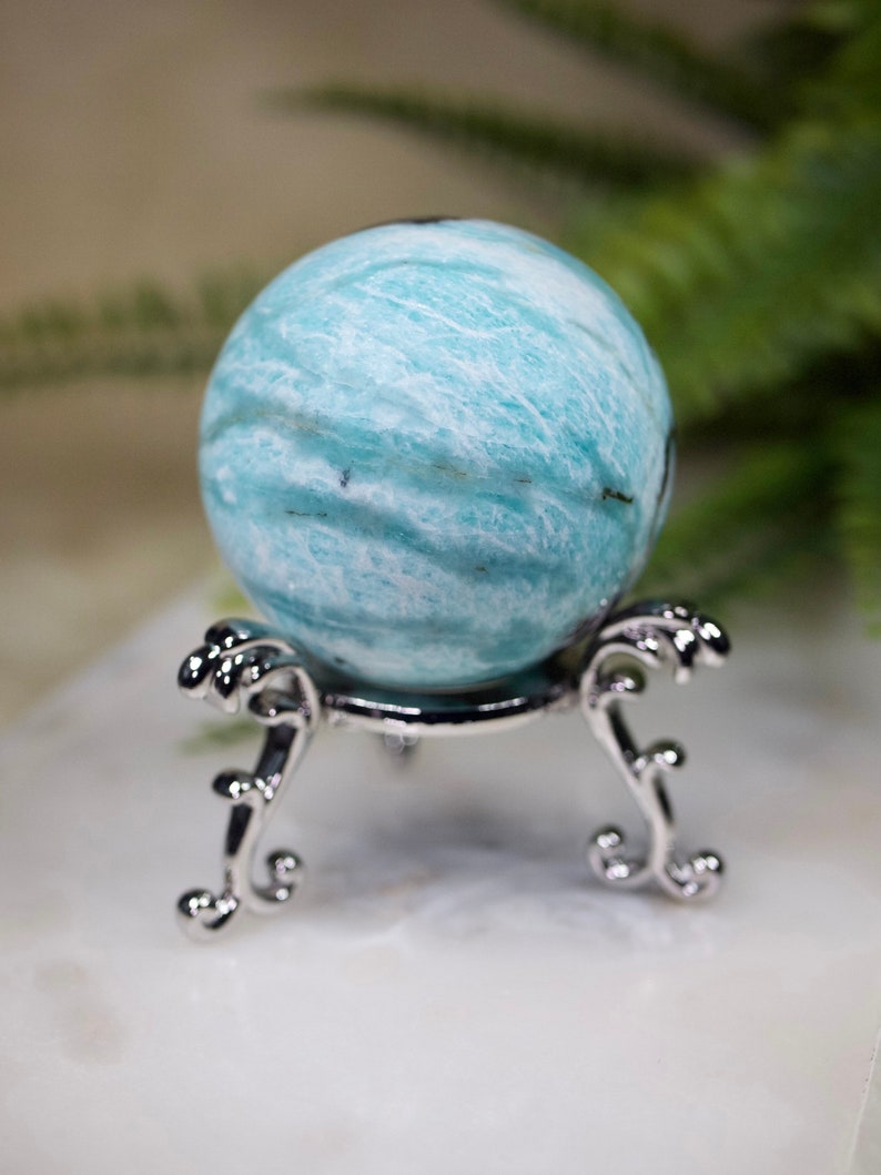 May include: A blue and white sphere of polished amazonite on a silver stand. The sphere has a swirling pattern of white and blue.
