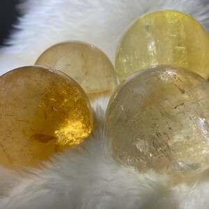 May include: Four yellow citrine crystal spheres of varying sizes on a white fluffy surface.