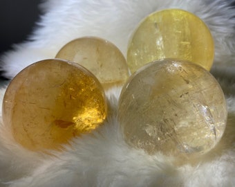 May include: Four yellow citrine crystal spheres of varying sizes on a white fluffy surface.