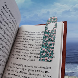 Peut inclure: Un marque-page rose et turquoise avec un motif floral. Le marque-page a une forme découpée en haut pour une insertion facile dans un livre.