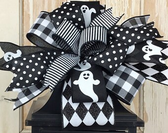 Könnte beinhalten: Schwarze und weiße Halloween-Laterne mit einer Schleife aus schwarz-weißem Punktmuster, Buffalo-Karo und gestreiftem Band. Die Schleife hat auch Geister-Ausschnitte. Die Laterne hat eine gelbe Kerze im Inneren.