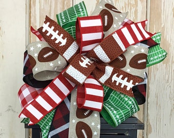 May include: A decorative bow featuring football-themed ribbons in various patterns, including footballs, stars, and a football field design. The bow is placed atop a black lantern with a yellow candle inside, creating a festive display.