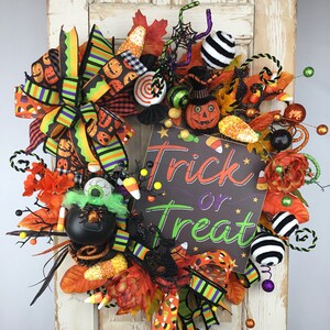 May include: A Halloween wreath with a black and green striped ribbon, orange and black candy corn, a black cauldron with a green eye, a black and white striped ball, and a sign that says "Trick or Treat".