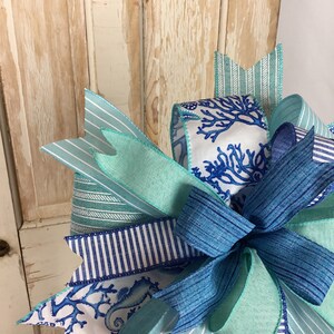 K&ouml;nnte beinhalten: Eine blaue und wei&szlig;e gestreifte Schleife mit einem Seepferdchen- und Korallendesign. Die Schleife ist mit einem blauen Band gebunden und hat einen gr&uuml;nen Bandakzent.