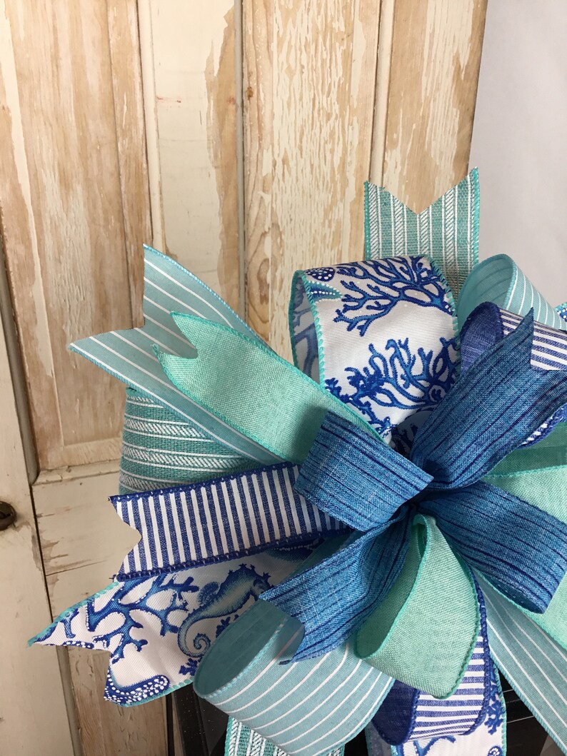 K&ouml;nnte beinhalten: Eine blaue und wei&szlig;e gestreifte Schleife mit einem Seepferdchen- und Korallendesign. Die Schleife ist mit einem blauen Band gebunden und hat einen gr&uuml;nen Bandakzent.