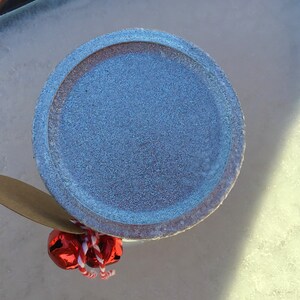 May include: A blue ceramic jar lid with a brown paper tag and red jingle bells attached.