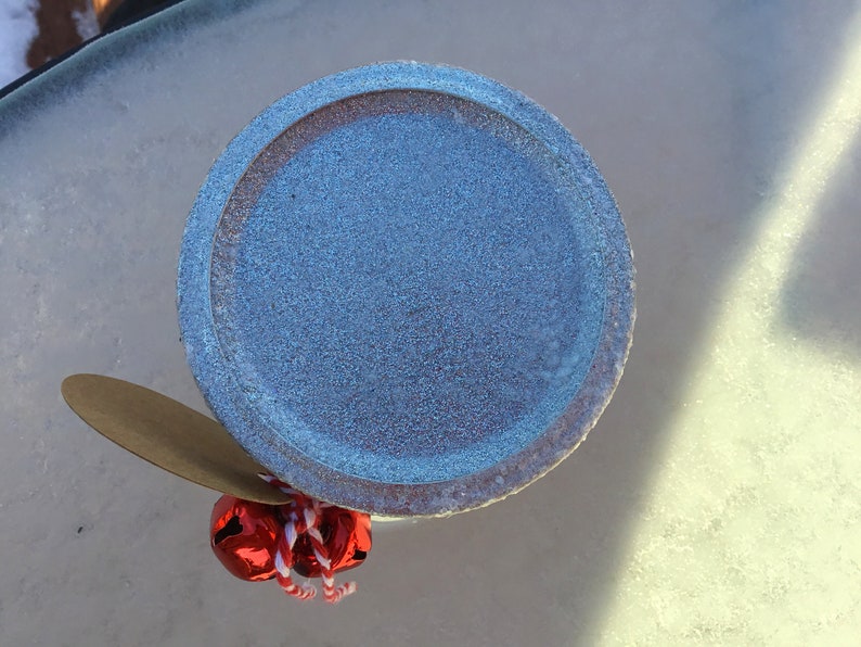 May include: A blue ceramic jar lid with a brown paper tag and red jingle bells attached.