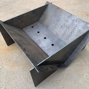 May include: A metal fire pit with a rectangular shape and a slightly angled design. The fire pit has a dark gray finish and several small holes in the bottom.