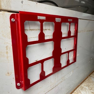 May include: A red metal storage rack with multiple compartments, mounted on a white wall. The rack has a rectangular shape and is secured with screws.