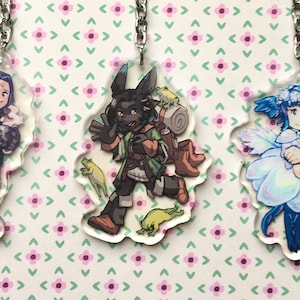 May include: Three acrylic keychains with cartoon character designs. The keychains feature characters with blue hair, a rabbit-like creature with a backpack, and a fairy-like figure with blue hair and a flower dress. Each keychain has a silver chain.