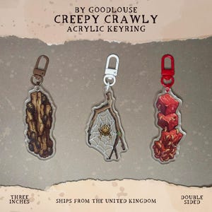 May include: Three acrylic keyrings with creepy crawly designs. One features a wood-like shape with bugs, another a spider in a web, and the third a stack of red cubes with a red base. Each keyring is approximately 3 inches in length.