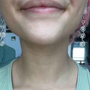 May include: A person wearing silver spiral earrings. The earrings are long and dangle from the earlobes.