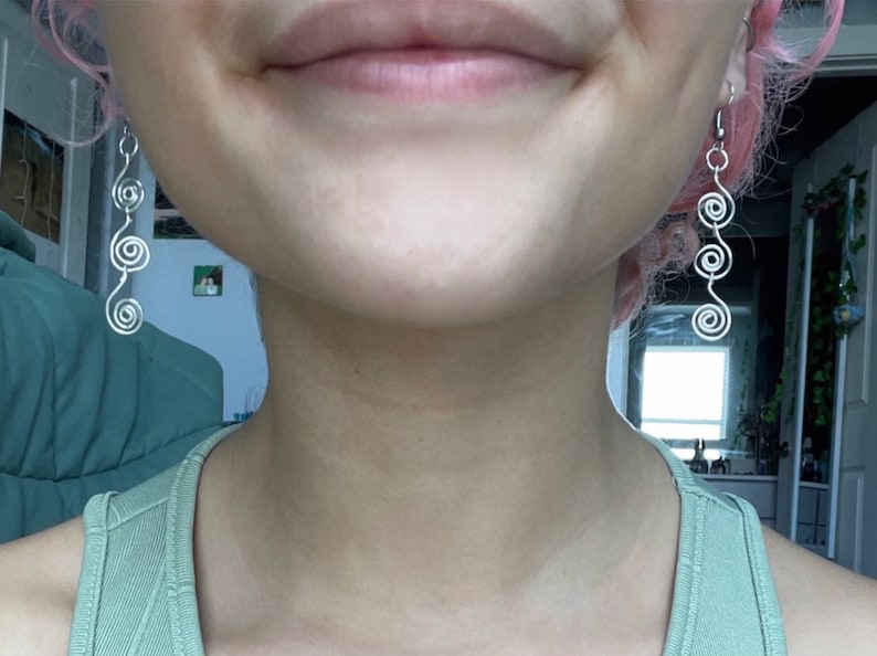 May include: A person wearing silver spiral earrings. The earrings are long and dangle from the earlobes.