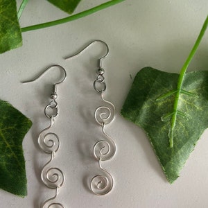 May include: A pair of silver dangle earrings with three spiral designs on each earring.