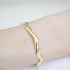 Può includere: Un braccialetto aperto dorato con forma ondulata.