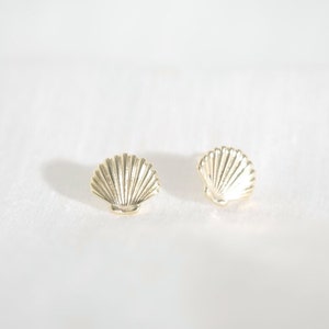 Op de afbeelding: Een paar gouden oorbellen met een schelpvorm. De oorbellen zijn klein en delicaat en hebben een eenvoudig, elegant ontwerp.