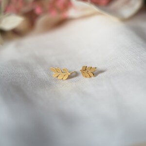 May include: A pair of gold leaf earrings. The earrings are small and delicate, and they feature a simple design of a single leaf.