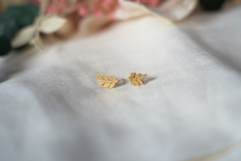 May include: A pair of gold leaf earrings. The earrings are small and delicate, and they feature a simple design of a single leaf.
