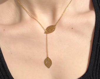 Könnte beinhalten: Eine goldene Halskette mit zwei blattartigen Anhängern. Die Kette ist zart und feminin.